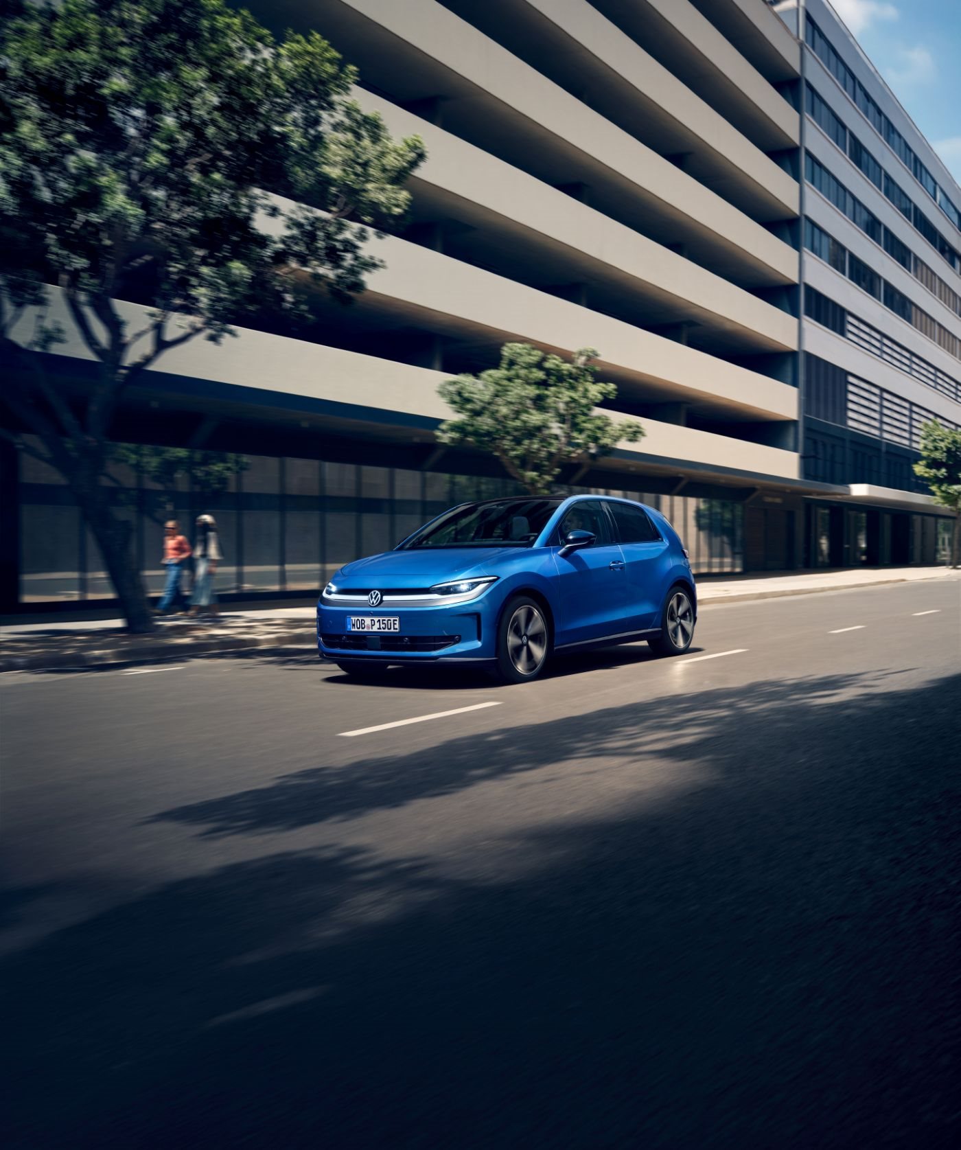 Blue Volkswagen ID. Polo driving past a modern city building
