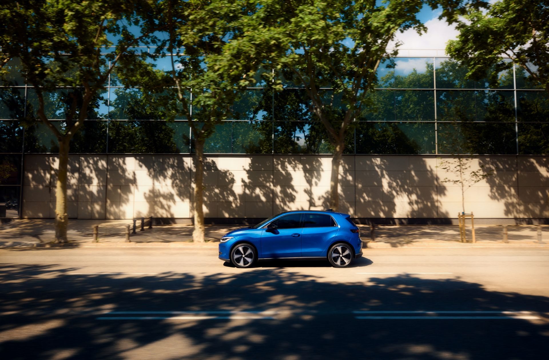 Side profile of a blue Volkswagen ID. Polo on a sunlit, tree-lined street